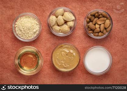 collection of almond super foods: nuts, flour, milk, oils and butter - top view of small glass bowls over orange textured bark paper