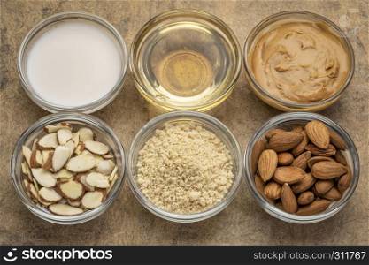 collection of almond super foods: nuts, flour, slices, milk, oils and butter - top view of small glass bowls over textured bark paper