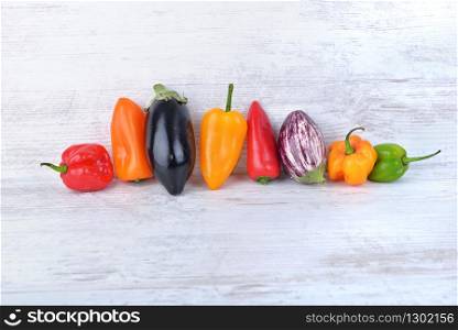 collection of colorful peppers and eggplants side by side on a white table