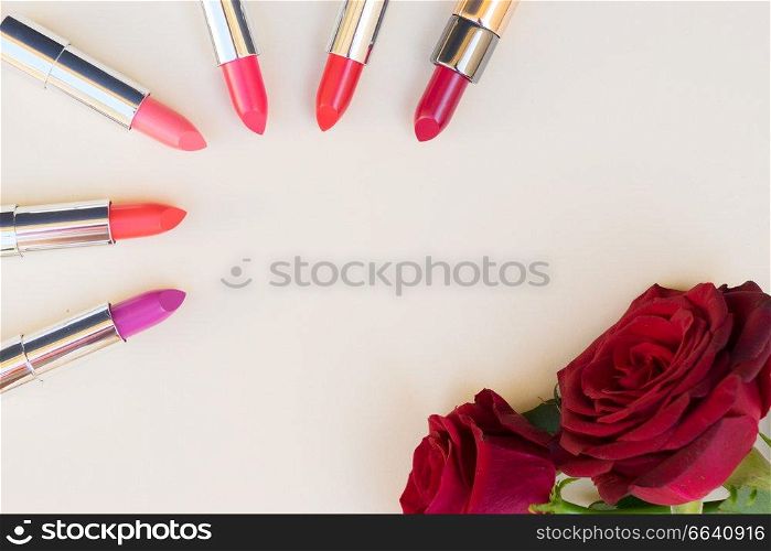 Collection of puple, pink and red shiny lipsticks and red roses, top view with copy space. Collection of lipsticks