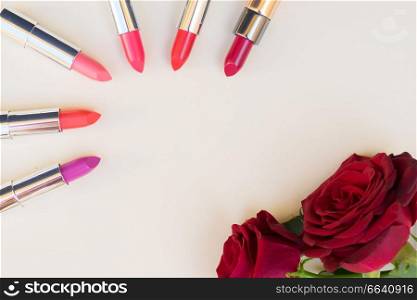 Collection of puple, pink and red shiny lipsticks and red roses, top view with copy space. Collection of lipsticks
