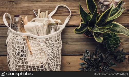 Collection of various succulent plants and Mesh market bag with bamboo cutlery, reusable bottles and eco cotton bags on wooden background. Sustainable lifestyle. Plastic free concept.