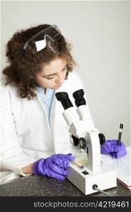 College age student examining a sample under the microscope and taking notes.