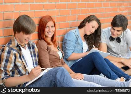 College students sitting in row against brick wall writing notes