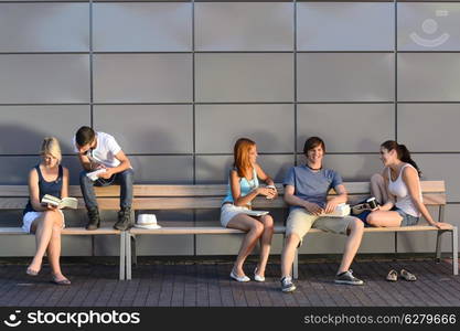 College students sitting on bench by modern wall outside campus