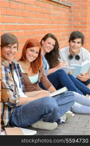 College students sitting on ground against brick wall holding books
