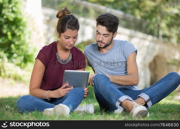 college students using tablet on campus lawn