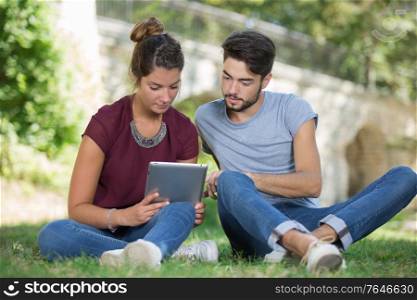 college students using tablet on campus lawn