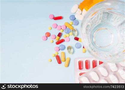 Coloful pills with glass of clear water close up over blue background with copy space. Medical pharmacy concept. Pile of pills