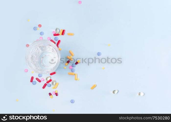 Coloful pills with glass of clear water over blue background with copy space. Medical pharmacy concept. Pile of pills