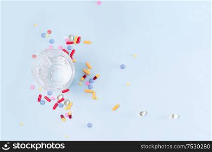 Coloful pills with glass of clear water over blue background with copy space. Medical pharmacy concept. Pile of pills