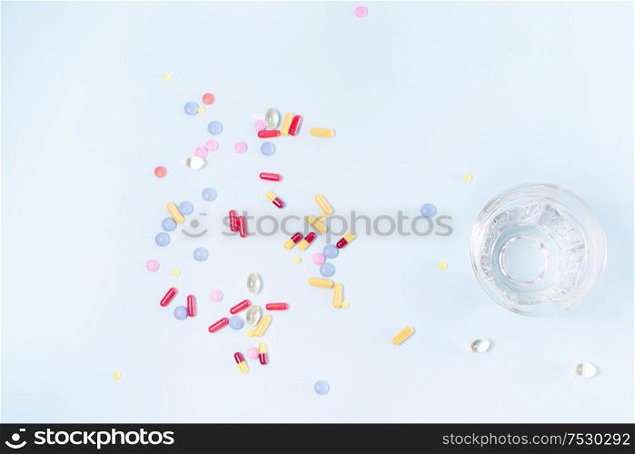 Coloful pills with glass of clear water over blue background with copy space, top view. Medical pharmacy concept. Pile of pills