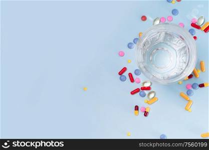 Coloful pills with glass of clear water over plain blue background with copy space. Medical pharmacy concept. Pile of pills