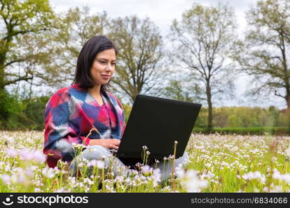 Colombian woman sits with laptop in meadow with cuckoo flowers