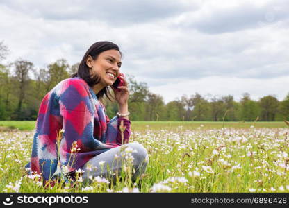 Colombian woman sitting in flowering meadow phoning with mobile phone