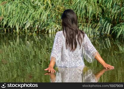 Colombian woman with black hair and white clothes walks in natural water