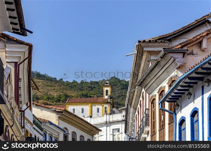 Colonial-style houses in the historic city of Ouro Preto in Minas Gerais with a church on top of the hill in the background.. Colonial-style houses in the historic city of Ouro Preto