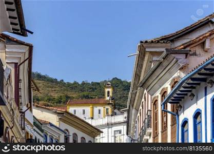 Colonial-style houses in the historic city of Ouro Preto in Minas Gerais with a church on top of the hill in the background.. Colonial-style houses in the historic city of Ouro Preto