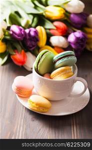 Color macaroons in a cup and flowers on the background. Color macaroons in a cup
