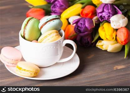 Color macaroons in a cup and flowers on the background. Color macaroons in a cup