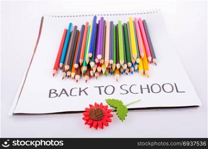 Color pencils and fake flower and on a notebook with a back to school title