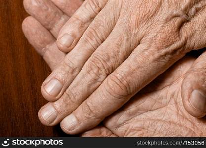 Color photo of senior man crossed hands detail on a dark wooden background