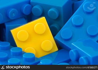 color toy background. yellow plastic brick in a middle of blue ones