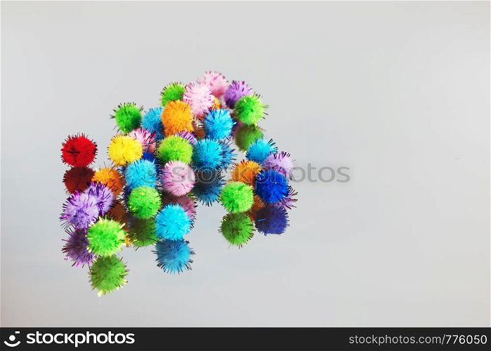 Colored beautiful pompons on a gray background. Assortment of pompons on the mirror surface.. Colored beautiful pompons on a gray background