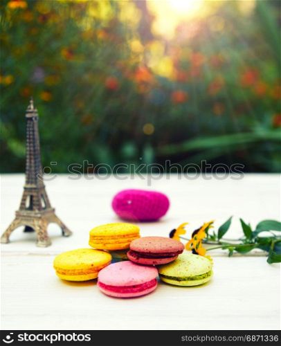 Colored cakes macarons on a white table, behind a bright sun shines through green bushes