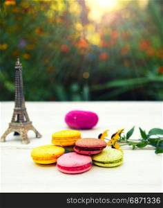 Colored cakes macarons on a white table, behind a bright sun shines through green bushes