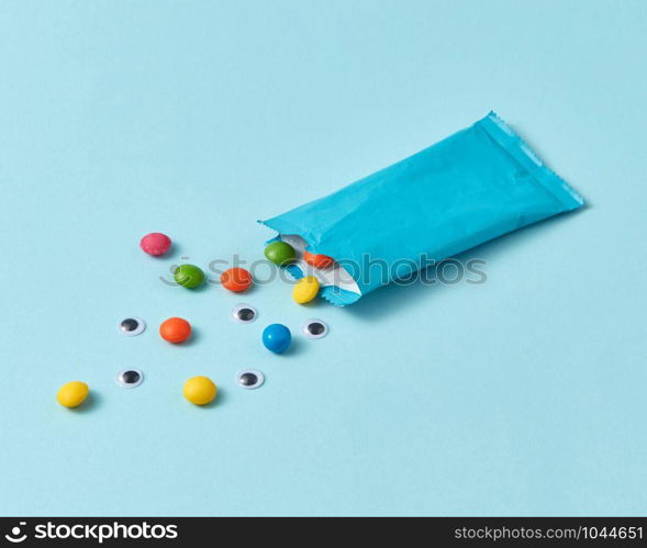 Colored candy and human pupils in a blue paper box on a light blue background, copy space. Halloween party treat.. Paper box with colorful candy and pupils on a light blue background.