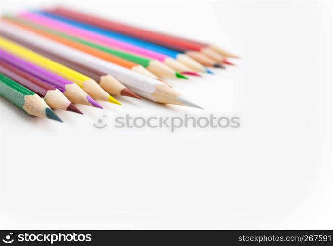 Colored crayon pencils in a row on the white desktop with selective focus on the white color tips with copy space. View from above.