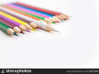 Colored crayon pencils in a row on the white desktop with selective focus on the white color tips with copy space. View from above.