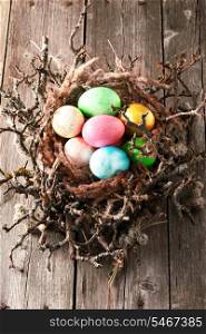 Colored easter eggs in nest on wooden table