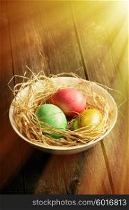 Colored easter eggs in nest on wooden table