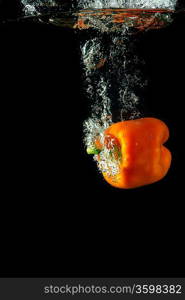 Colored orange paprika in water splashes on black background