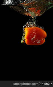 Colored orange paprika in water splashes on black background