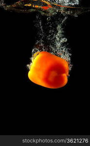 Colored orange paprika in water splashes on black background