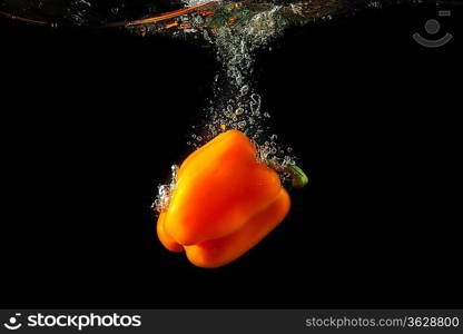 Colored orange paprika in water splashes on black background