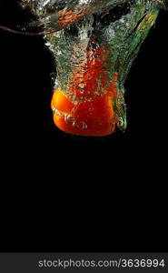 Colored orange paprika in water splashes on black background