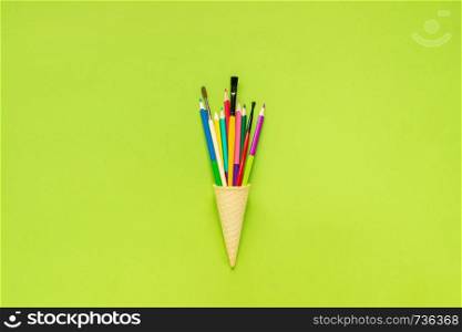 Colored pencils paintbrush in waffle ice cream cone on green paper background. Concept Education or Back to school Flat lay Top view Template for postcard, lettering text or your design.. Colored pencils paintbrush in waffle ice cream cone on green paper background. Concept Education or Back to school Flat lay Top view Template for postcard, lettering text or your design