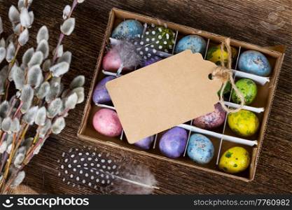 Colored quail eggs with feather and catkins on wood, copy space on paper note. Colored quail eggs 