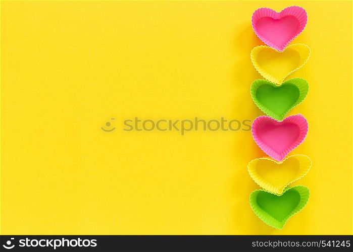 Colored silicone heart shaped molds dish for baking cupcakes lined in rowright side on yellow paper background. Template for lettering, text or your design Top view, copy space.. Colored silicone heart shaped molds dish for baking cupcakes lined in row right side on yellow paper background. Template for lettering, text or your design Top view, copy space