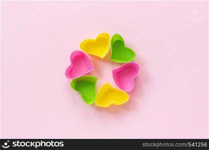 Colored silicone heart shaped molds dish for baking cupcakes on pink paper background. Template for lettering, text or your design Top view, copy space.. Colored silicone heart shaped molds dish for baking cupcakes on pink paper background. Template for lettering, text or your design Top view, copy space