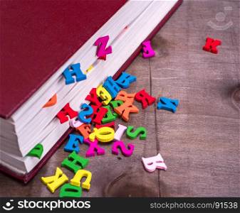 colored wooden letters fall out of a closed book in a red cover