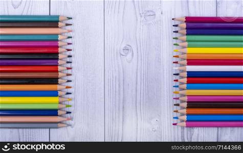 colored wooden pencils, facing each other, on a gray and white wooden background