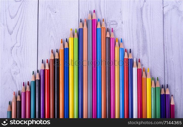 colored wooden pencils, forming a triangle, on a white and gray wooden background