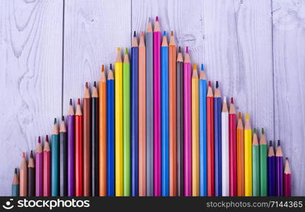 colored wooden pencils, forming a triangle, on a white and gray wooden background