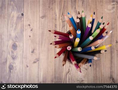 colored wooden pencils, in a brown leather beaker, seen from above, with wooden background