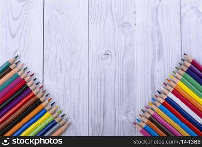colored wooden pencils, in the bottom corners of a white and gray wooden background